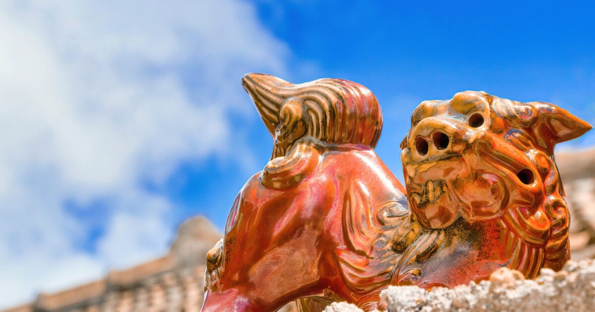 青空の下に並ぶ光沢のある赤いシーサー像