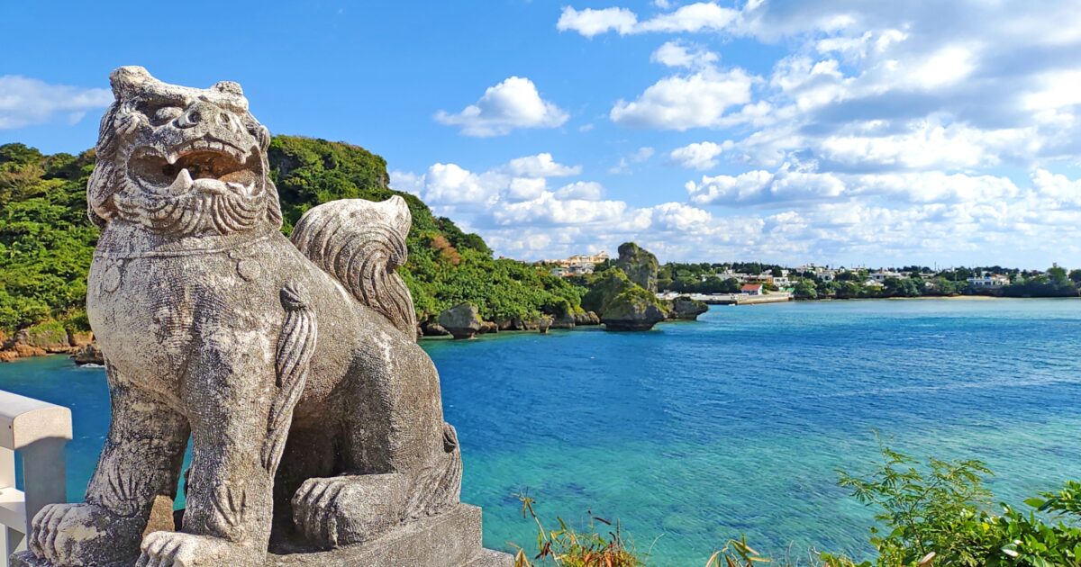 青い海を見下ろす石造りのシーサー像